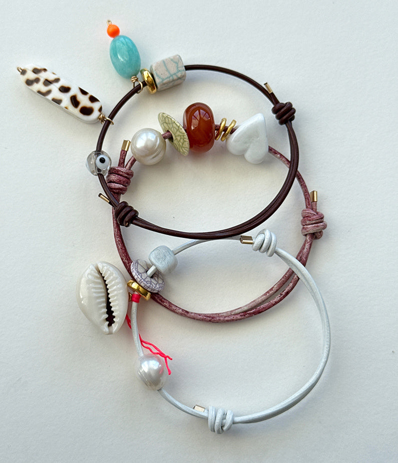 Three bracelets with various beads and shells on a light background
